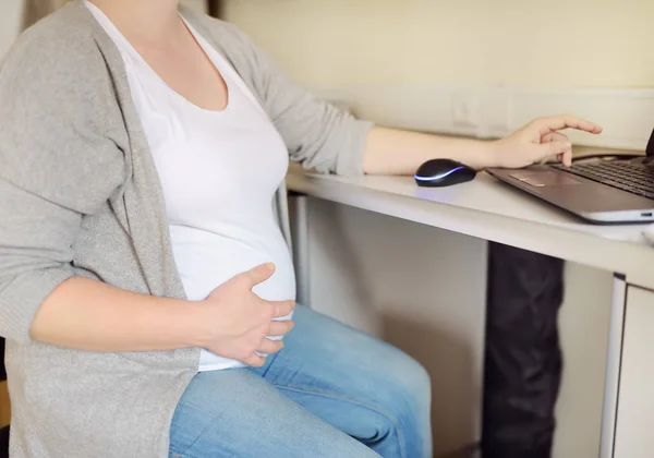 Kobieta w ciąży pracuje na laptopie w jej miejscu pracy w biurze. Ubezpieczenie zdrowotne w wieku rozrodczym. Urlop macierzyński. Ciąża i praca. — Zdjęcie stockowe