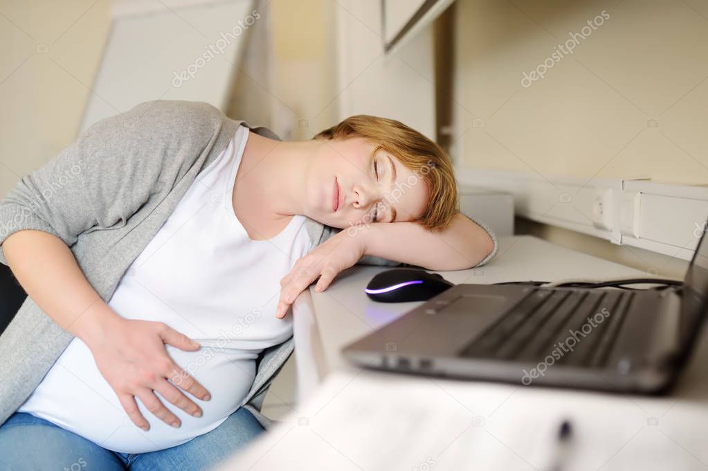 Tired pregnant woman sleeping near laptop at her working place in office. Medical insurance childbearing. Maternity leave. Pregnancy and work.