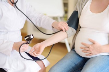 Jinekolog doktor hamile bir kadının baskısını ölçer. Sağlık sigortası çocuk doğurma. Gebelik için aile doktoru. Doğum izni.