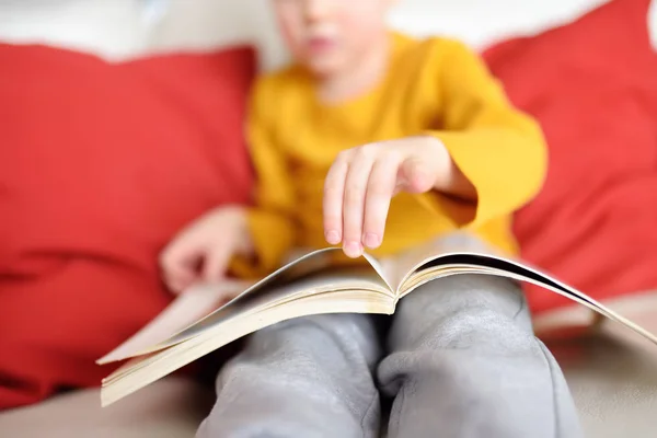 Little boy is sitting at home on the couch and reading a book. Learning to read. — Stock Photo, Image