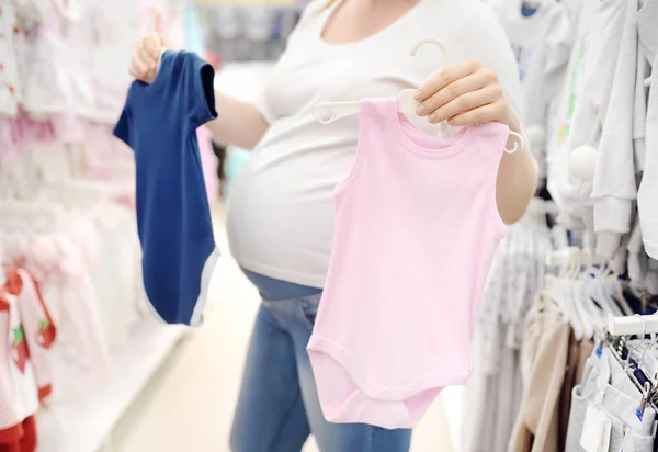 Jovem grávida escolhendo roupas rosa ou azul na loja para recém-nascidos — Fotografia de Stock