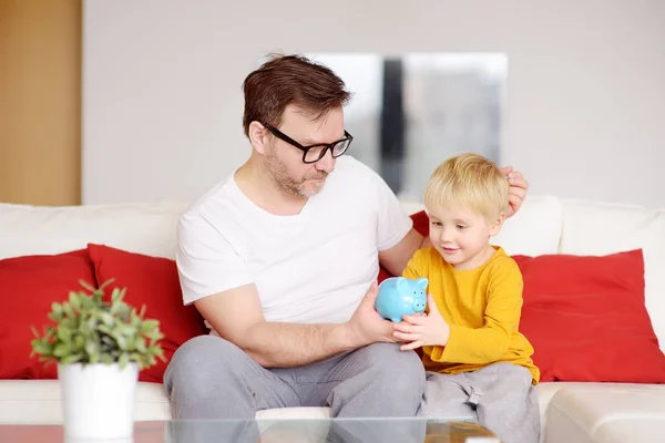Father and son putting coin into piggy bank. Education of children in financial literacy. — Stock Photo, Image