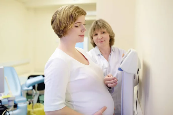 Врач-гинеколог измеряет вес беременной женщины. Медицинская страховка. Семейный врач для беременности. Отпуск по беременности . — стоковое фото