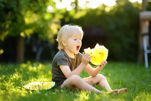 Niño caucásico con pelos rubios comiendo sandía amarilla en el patio trasero —  Fotos de Stock