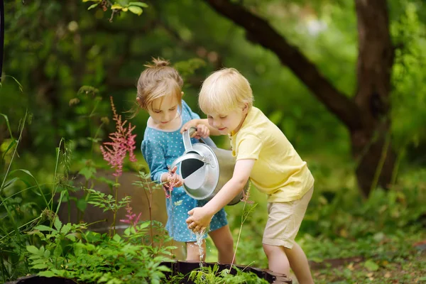 Roztomilá chlapeček a děvče zalévání v zahradě v letním slunném dnu. Maminky malý pomocníci. — Stock fotografie