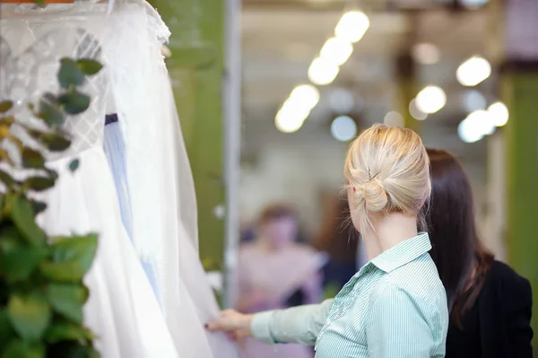 Qualche bel vestito da sposa su un appendiabiti. Due giovane donna sta scegliendo l'abito da sposa perfetto durante lo shopping nuziale . — Foto Stock