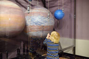 Little caucasian boy is looking an exposition in a scientific museum. Models of planets of the solar system. Activities for family with preschooler kids. clipart