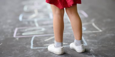 Küçük kızın bacaklarının yakın çekim ve hopscotch asfalt çizilmiş. Çocuk güneşli bir günde oyun açık havada hopscotch oyunu oynuyor.