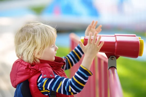 Mignon petit blond caucasien garçon, enfant ou enfant regarder à travers jumelles sur aire de jeux en plein air — Photo