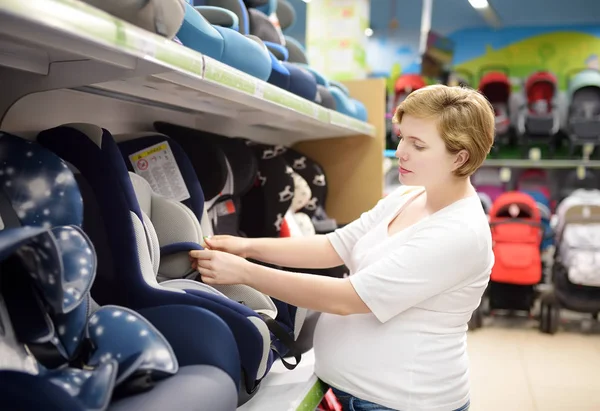 Νεαρή όμορφη έγκυος γυναίκα διαλέγει παιδικό κάθισμα αυτοκινήτου. Ψώνια για μέλλουσες μητέρες και το μωρό. — Φωτογραφία Αρχείου