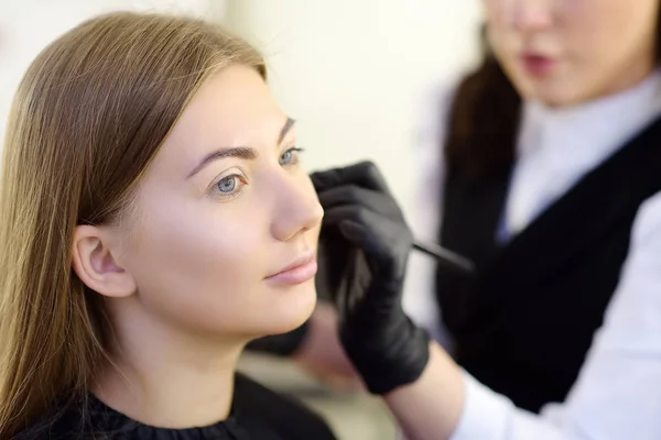 Esthéticienne appliquant le ton de la fondation à l'aide d'un pinceau spécial sur le visage jeune beau modèle. Soins du visage et maquillage — Photo