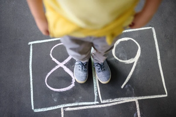 Closeup of little boy's legs and hopscotch drawn on asphalt. Child playing hopscotch game on playground outdoors on a sunny day. — Stock Photo, Image