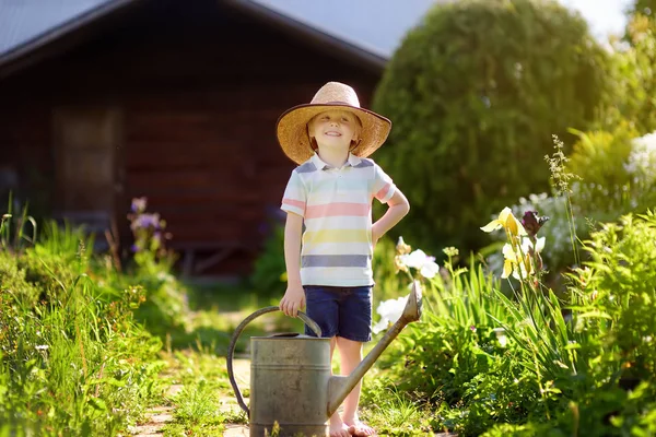Milý chlapeček zalévání rostlin v zahradě na letní slunečný den. — Stock fotografie