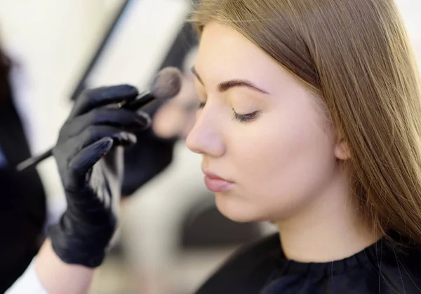 Maquiagem artista aplicando o tom da fundação usando escova especial no rosto jovem modelo bonito. Cuidados faciais e maquiagem — Fotografia de Stock