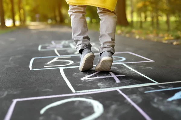Closeup of little boy\'s legs and hopscotch drawn on asphalt. Child playing hopscotch game on playground outdoors on a sunny day.