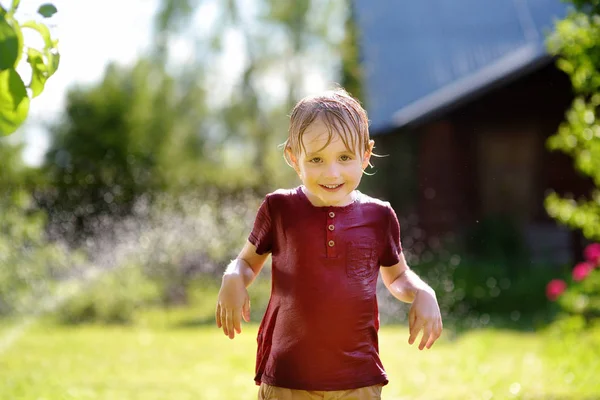 Engraçado menino brincando com aspersor de jardim no quintal ensolarado — Fotografia de Stock