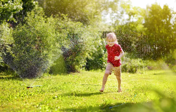 Chico divertido jugando con aspersor de jardín en el patio trasero soleado —  Fotos de Stock