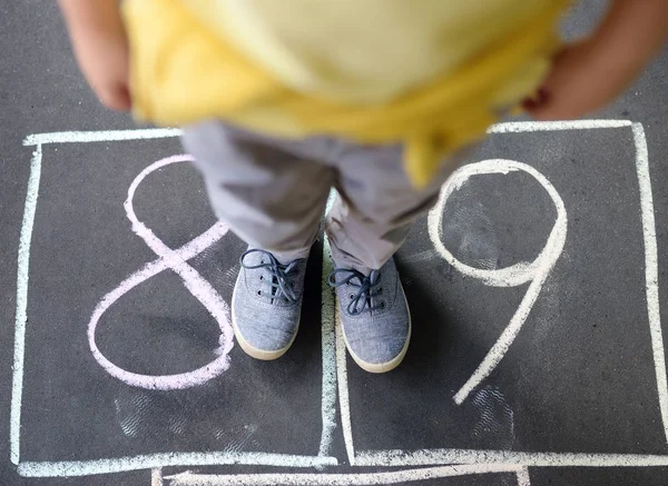 Closeup of little boy's legs and hopscotch drawn on asphalt. Child playing hopscotch game on playground outdoors on a sunny day. — Stock Photo, Image