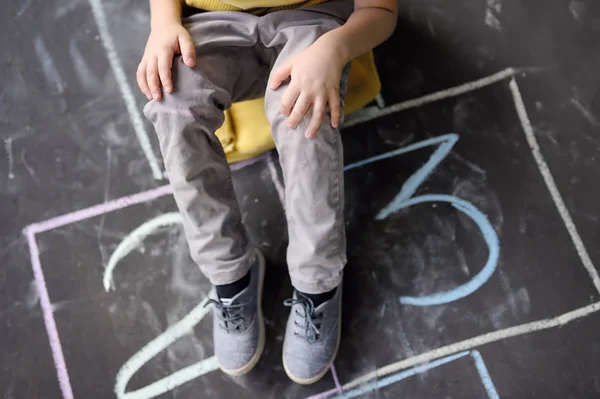 Primo piano delle gambe del bambino e tramoggia disegnata su asfalto. Bambino che gioca a hopscotch nel parco giochi all'aperto in una giornata di sole . — Foto Stock