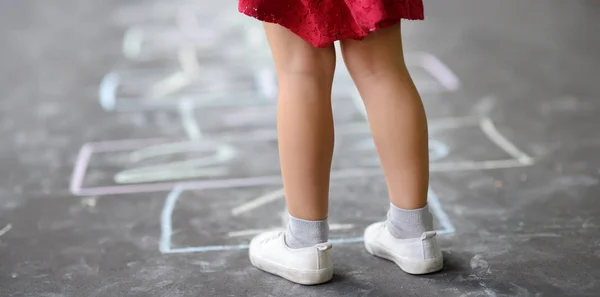 Close-up van kleine meisje benen en Hinkelspel getrokken op asfalt. Kind spelen Hinkelspel spel op Speeltuin buitenshuis op een zonnige dag. — Stockfoto