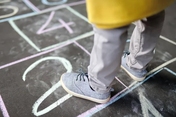 Closeup of little boy's legs and hopscotch drawn on asphalt. Child playing hopscotch game on playground outdoors on a sunny day. — Stock Photo, Image