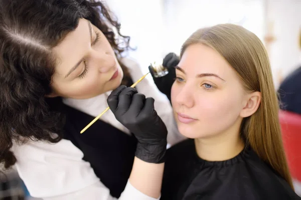 Cosmetologist painting eyebrows by brush. Attractive woman getting facial care and makeup at beauty salon. Architecture eyebrows.