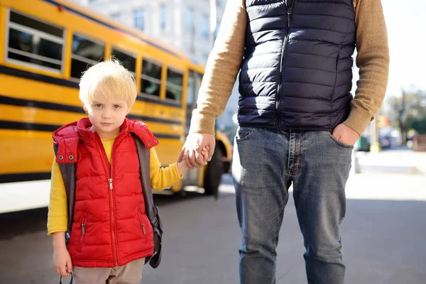 Elementary student hold hands his father near yellow school bus on background. — Stock Photo, Image