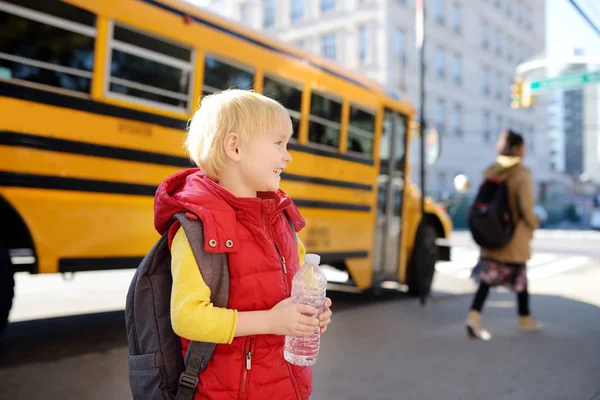 Pupil with schoolbag and bottle of water with yellow school bus on background. — Stock Photo, Image