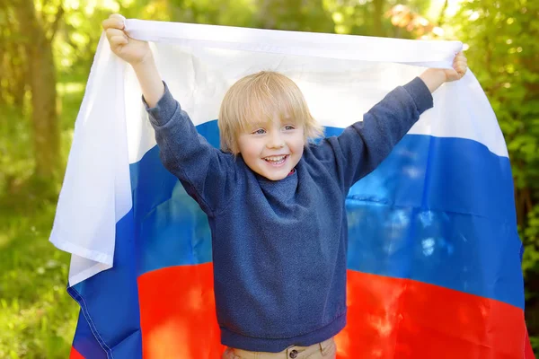 Retrato de menino bonito no parque de verão público com bandeira russa no fundo. Fãs criança apoiando e torcendo sua equipe nacional. Dia de independência . — Fotografia de Stock