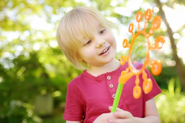 Menino bonito está brincando com grandes bolhas ao ar livre. Criança está soprando bolhas grandes e pequenas simultaneamente . — Fotografia de Stock