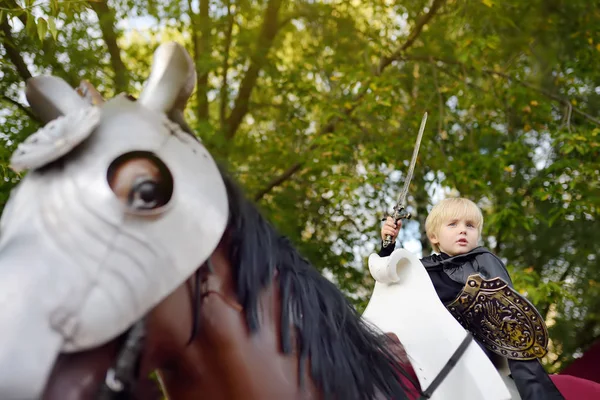 Портрет милого маленького хлопчика, одягненого як середньовічний лицар з мечем і щитом, що катається на коні — стокове фото