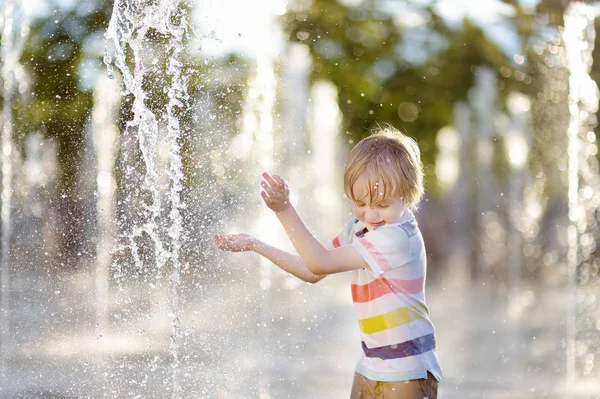 Petit garçon joue sur la place entre les jets d'eau dans la fontaine à la journée ensoleillée d'été . — Photo