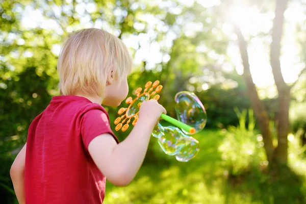 Lindo niño está jugando con grandes burbujas al aire libre. Niño está soplando burbujas grandes y pequeñas simultáneamente . — Foto de Stock