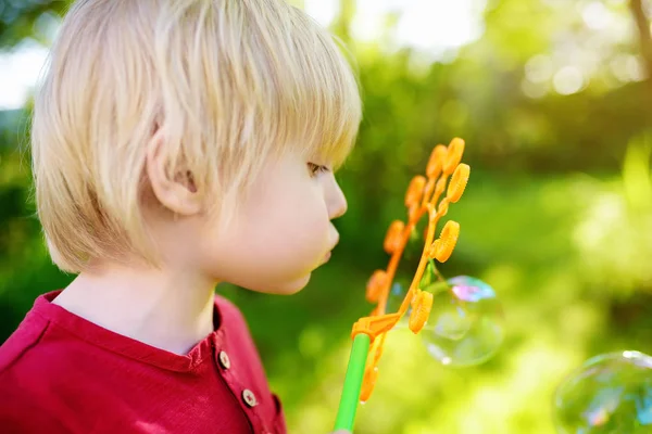 Cute little boy is playing with big bubbles outdoor. Child is blowing big and small bubbles simultaneously.