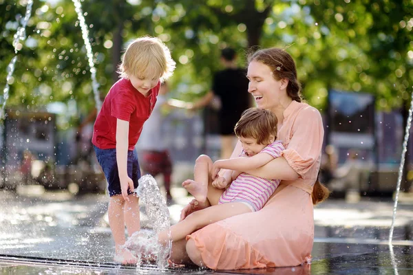 Matka z niepełnosprawną dziewczyną i chłopcem bawią się na fontannie w słonecznym letnim parku. Dziecięcym porażeniem mózgowym. Rodzina z niepełnosprawnym dzieckiem. — Zdjęcie stockowe