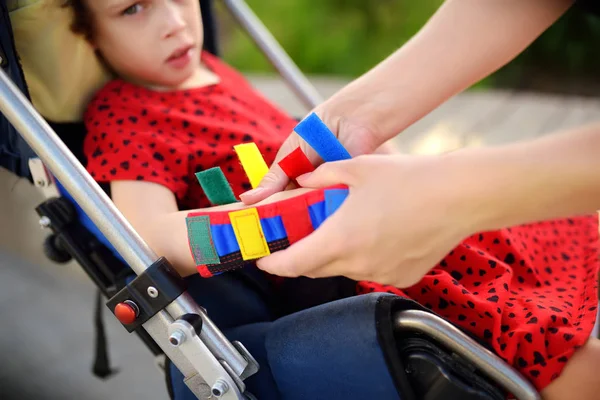 Moeder zet orthese op haar dochter armen. Gehandicapte meisje zittend op een rolstoel. Kind cerebrale parese. — Stockfoto