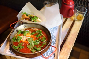 Shakshuka İsrail mutfağının kafede tepside. Shakshouka domates, sebze ve otlar ile kızarmış yumurta.