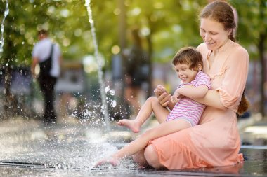 Güneşli yaz gününde parkÇeşme eğlenen annesinin kollarında güzel engelli kız portresi. Çocuk serebral palsi.