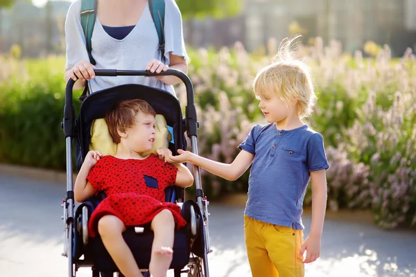 Frau mit einem Jungen und einem behinderten Mädchen im Rollstuhl, die im Sommer im Park spazieren gehen. Zerebralparese bei Kindern. Familie mit behindertem Kind. — Stockfoto