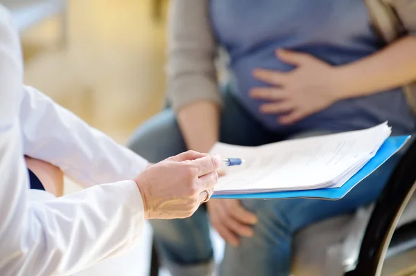 La mujer embarazada firma el contrato o permiso durante la aceptación del médico ginecólogo. Seguro médico de maternidad. Médico de familia para la gestación. Permiso de maternidad . — Foto de Stock
