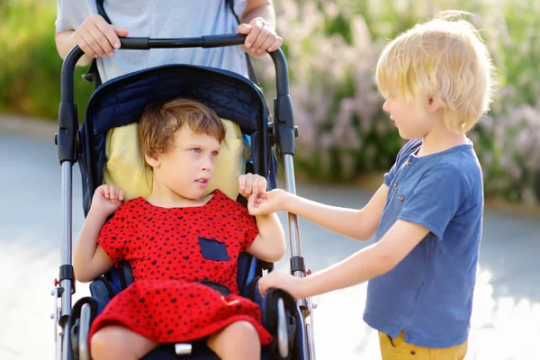 Une femme avec un garçon et une fille handicapée dans un fauteuil roulant marchant dans le parc l'été. La paralysie cérébrale infantile. Famille avec enfant handicapé . — Photo