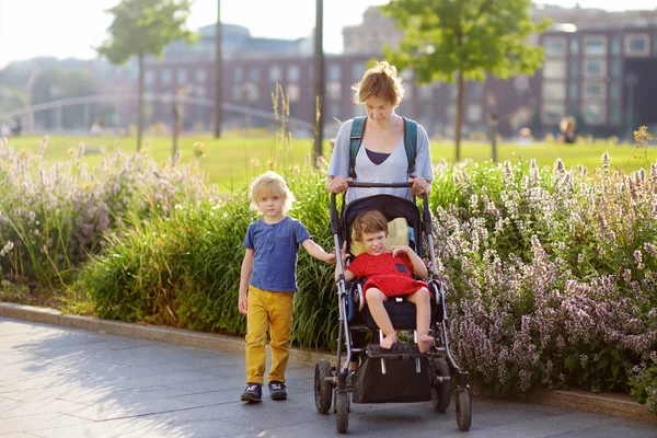 Mulher com um menino e uma menina deficiente em uma cadeira de rodas andando no parque no verão. Paralisia cerebral infantil. Família com criança com deficiência . — Fotografia de Stock