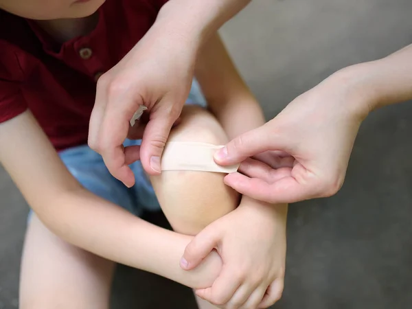 Mãe mãos aplicando gesso adesivo médico antibacteriano no joelho da criança depois de cair . — Fotografia de Stock