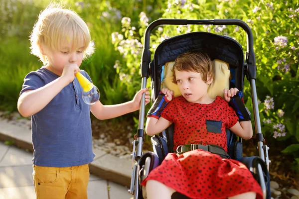 Menino e uma menina deficiente brincando juntos no parque de verão. Paralisia cerebral infantil. Família com criança com deficiência . — Fotografia de Stock