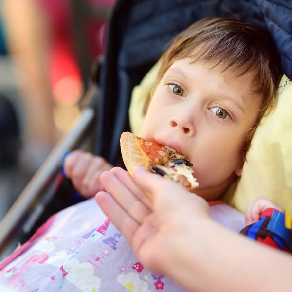 Mother feeding pizza's a little disabled girl in a wheelchair. Child cerebral palsy. Inclusion. — Stock Photo, Image