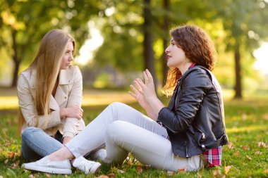 Güneşli parkta yerde otururken konuşan iki güzel genç kadın. Kız.