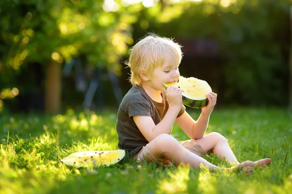 Caucasiano menino com cabelos loiros comendo melancia amarela no quintal — Fotografia de Stock