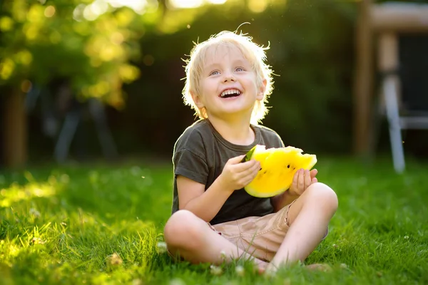 Kaukaski mały chłopiec z blond włosami jedzenia żółty arbuz na podwórku — Zdjęcie stockowe