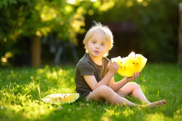 Niño caucásico con pelos rubios comiendo sandía amarilla en el patio trasero — Foto de Stock