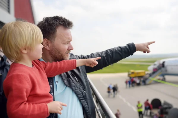 Lindo niño y su padre apuntando a los aviones en la cubierta de observación en el aeropuerto de la pequeña ciudad europea antes del vuelo. Un pasajero encantador esperando el embarque. Viajes en familia con concepto infantil — Foto de Stock
